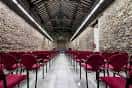 Sala interior del palacio acondicionada para eventos con filas de sillas rojas y paredes de piedra