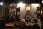 Interior del bar con clientes sentados en mesas, capturando el ambiente nocturno
