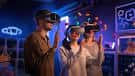 Tres personas utilizando gafas de realidad virtual en un entorno de juego iluminado con luces de neón