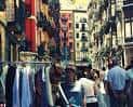 Escena del mercado de segunda mano en la Calle Dos de Mayo, con puestos de ropa y edificios coloridos al fondo