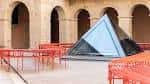 Patio interior con estructura piramidal de vidrio y arquería de piedra