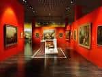 Interior de una sala de exposiciones con paredes de color rojo y cuadros clásicos