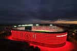 Perspectiva nocturna del estadio con la estructura exterior iluminada intensamente en rojo