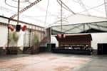 Interior amplio de la sala de eventos con escenario, zona de barra y techo de estructura metálica