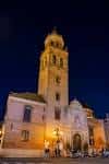 Vista nocturna iluminada de la torre y la fachada de la Parroquia de San Pedro
