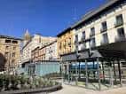 Panorámica de la plaza con edificios residenciales y estructuras de acceso acristaladas
