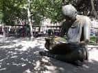 Escultura de la niña leyendo situada en una zona ajardinada de la plaza