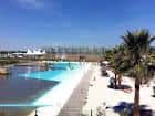 Zona de playa urbana con arena blanca, palmeras y piscina de aguas cristalinas