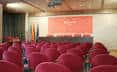 Salón de actos con filas de butacas rojas y mesa presidencial para eventos