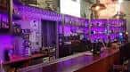 Barra de bar con iluminación ambiental en tonos púrpuras y estanterías de cristal