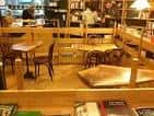 Zona de cafetería y lectura con mesas y sillas de madera dentro del local