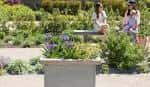 Visitantes descansando en un banco rodeado de vegetación y flores en los jardines de One Garden Brighton