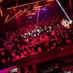 Ambiente de la sala con público y juegos de luces rojas durante un evento