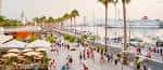 Paseo marítimo de Muelle Uno con zonas de restauración, palmeras y barcos al atardecer