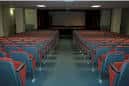 Interior del salón de actos con filas de butacas y escenario al fondo
