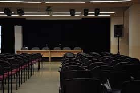 Salón de actos equipado con escenario y filas de butacas para eventos