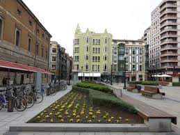 Perspectiva de la plaza con zonas ajardinadas, bancos y edificios residenciales