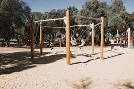 Área de columpios de madera en una zona recreativa sombreada por árboles