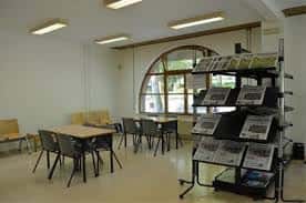 Zona de consulta con mesas de estudio y expositor de prensa