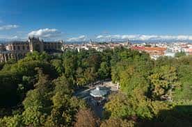 Vista aérea de un parque arbolado con un quiosco central y la ciudad al fondo
