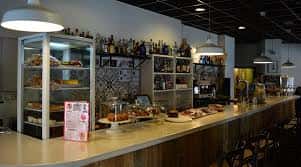 Vista de la barra del local con vitrina de repostería y estanterías de licores