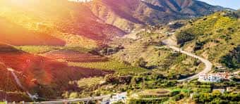 Paisaje montañoso de los Montes de Málaga con campos de cultivo y caminos serpenteantes bajo la luz del atardecer