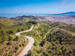 Vista aérea de la carretera de montaña atravesando el bosque con la ciudad de Málaga y el mar al fondo