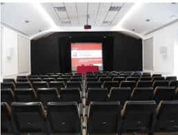 Salón de actos con filas de asientos y pantalla para conferencias y presentaciones