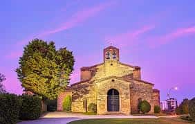 Vista exterior de la iglesia prerrománica iluminada durante el atardecer
