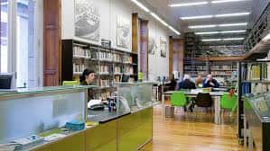 Interior de la biblioteca con zona de atención al público y puestos de lectura