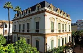 Vista en perspectiva del edificio histórico destacando su arquitectura y entorno ajardinado
