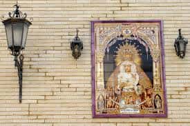 Retablo cerámico devocional y faroles de forja sobre la fachada de ladrillo visto