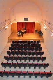 Vista aérea del auditorio de la escuela con piano de cola en el escenario y filas de butacas