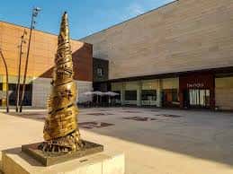 Plaza exterior del centro con escultura contemporánea y zona de terraza
