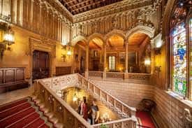 Interior del palacio con gran escalera señorial y detalles arquitectónicos neogóticos