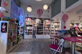Interior de la librería con estanterías blancas, mesas de lectura y decoración de globos colgantes