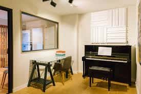 Estudio de práctica con piano de pared, escritorio y paneles de acondicionamiento acústico
