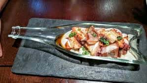 Ración de pulpo presentada de forma creativa en un plato de cristal con forma de botella