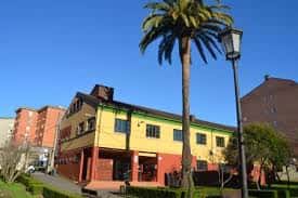 Vista exterior del edificio rodeado de zonas verdes y una palmera