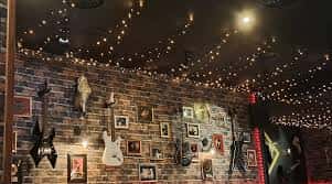 Interior del bar con pared de ladrillo decorada con guitarras y techo con guirnaldas de luces