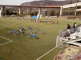 Vista del campo de fútbol exterior y gradas del polideportivo con un puente al fondo