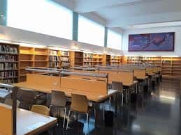Interior de la biblioteca de la facultad con puestos de lectura y estanterías de libros