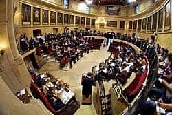 Interior del salón de plenos con disposición semicircular y retratos históricos