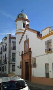 Vista exterior de la fachada blanca y la torre campanario de la parroquia