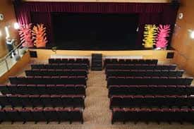 Escenario del teatro con telón granate y filas de asientos en primer plano