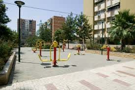 Área de gimnasio al aire libre con equipos de ejercicio en una plaza pública de la barriada