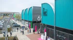 Pasillo peatonal del centro comercial con edificios de diseño industrial en tonos azules y zonas de paseo