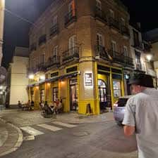 Vista exterior nocturna del Bar La Ilustre y su terraza en una esquina de Sevilla
