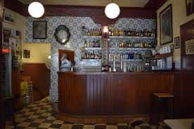 Vista de la barra de madera clásica y estanterías con botellas en el interior del café