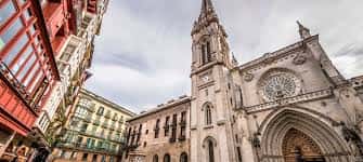Vista panorámica de la Catedral de Santiago desde la calle, con edificios coloridos a los lados y cielo nublado